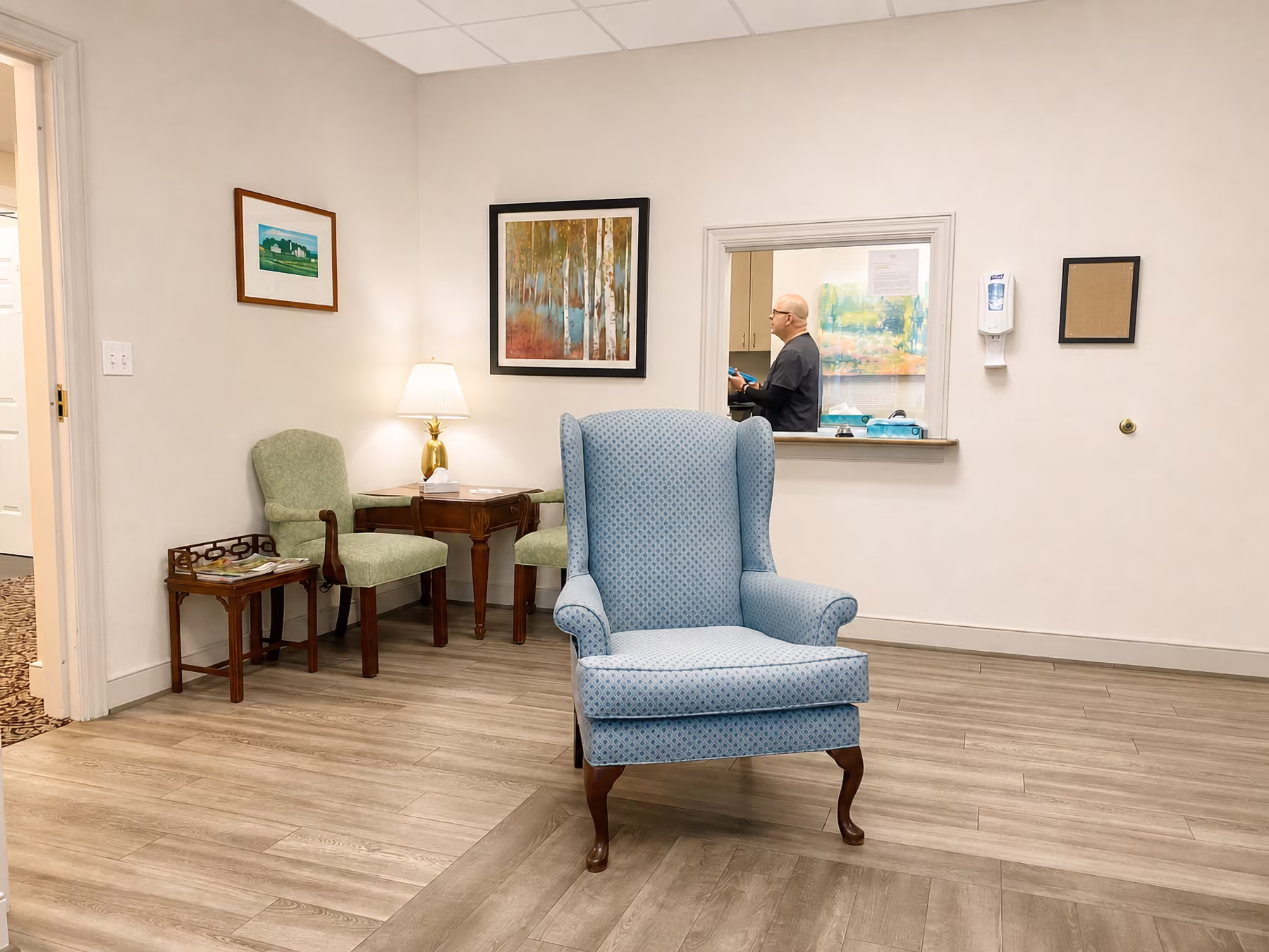 A man stands at a reception desk in a waiting area with a blue chair in front.