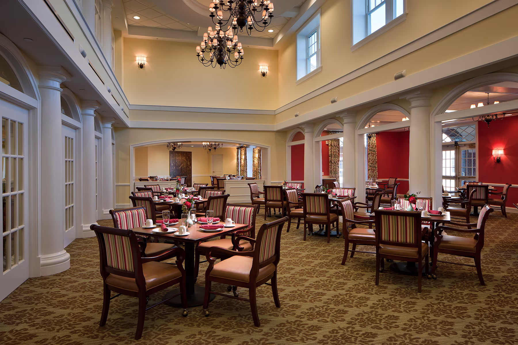 A dining room with neatly set tables and chairs, featuring elegant lighting and high ceilings.