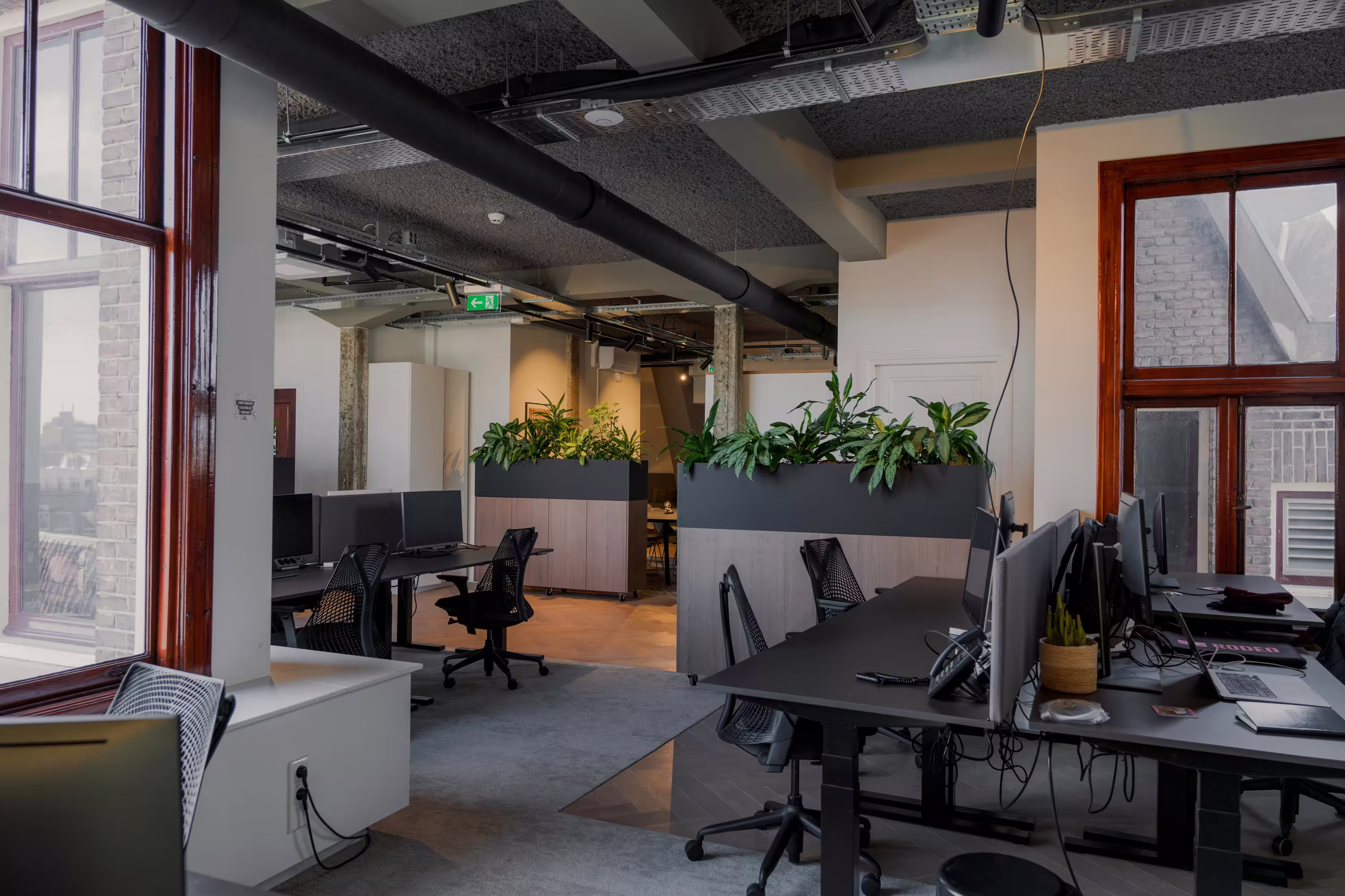 Man and woman having a professional conversation across a round wooden table in a bright, modern office with plants.