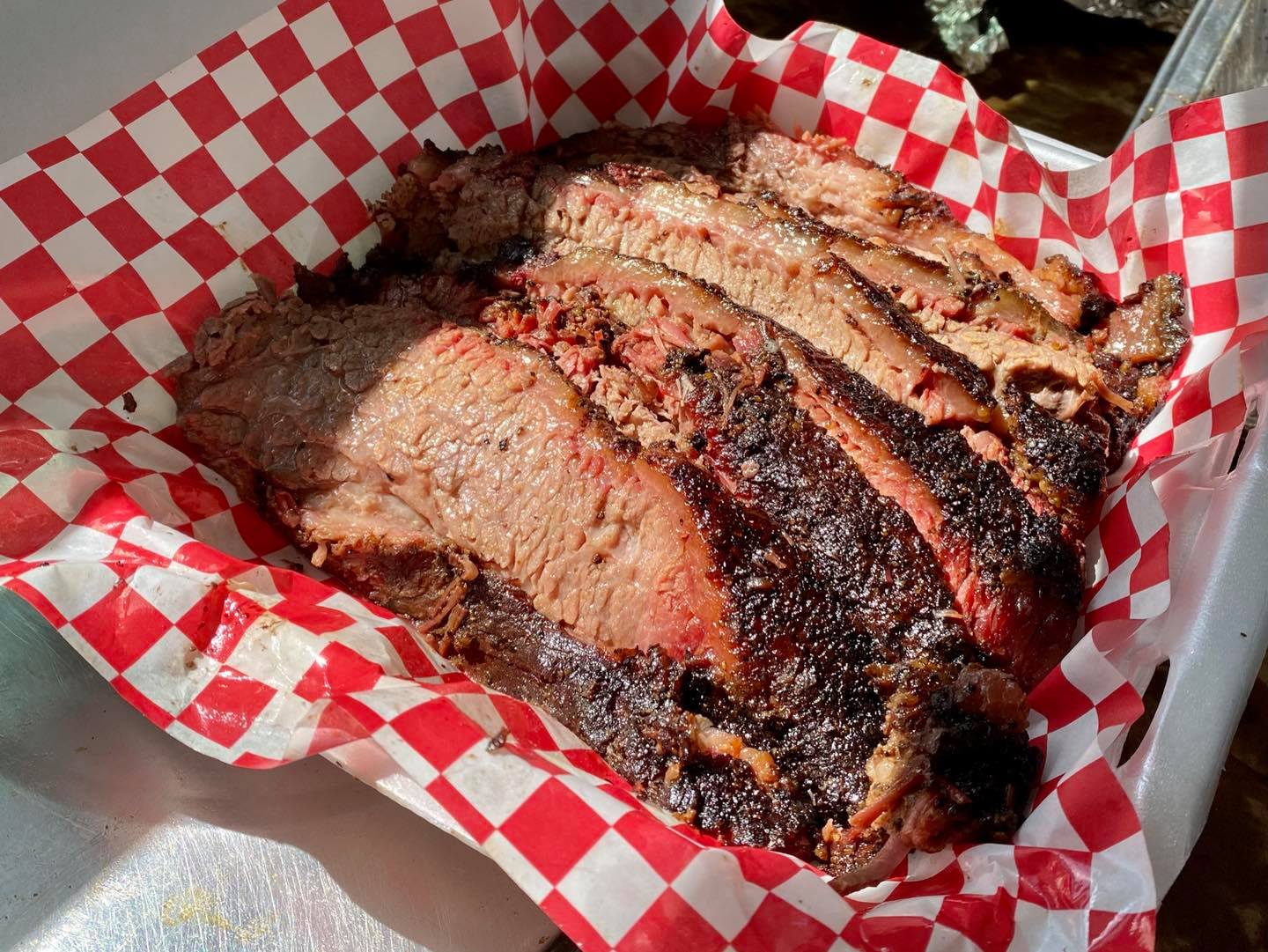 A large piece of meat is sitting in a red and white checkered paper bag.