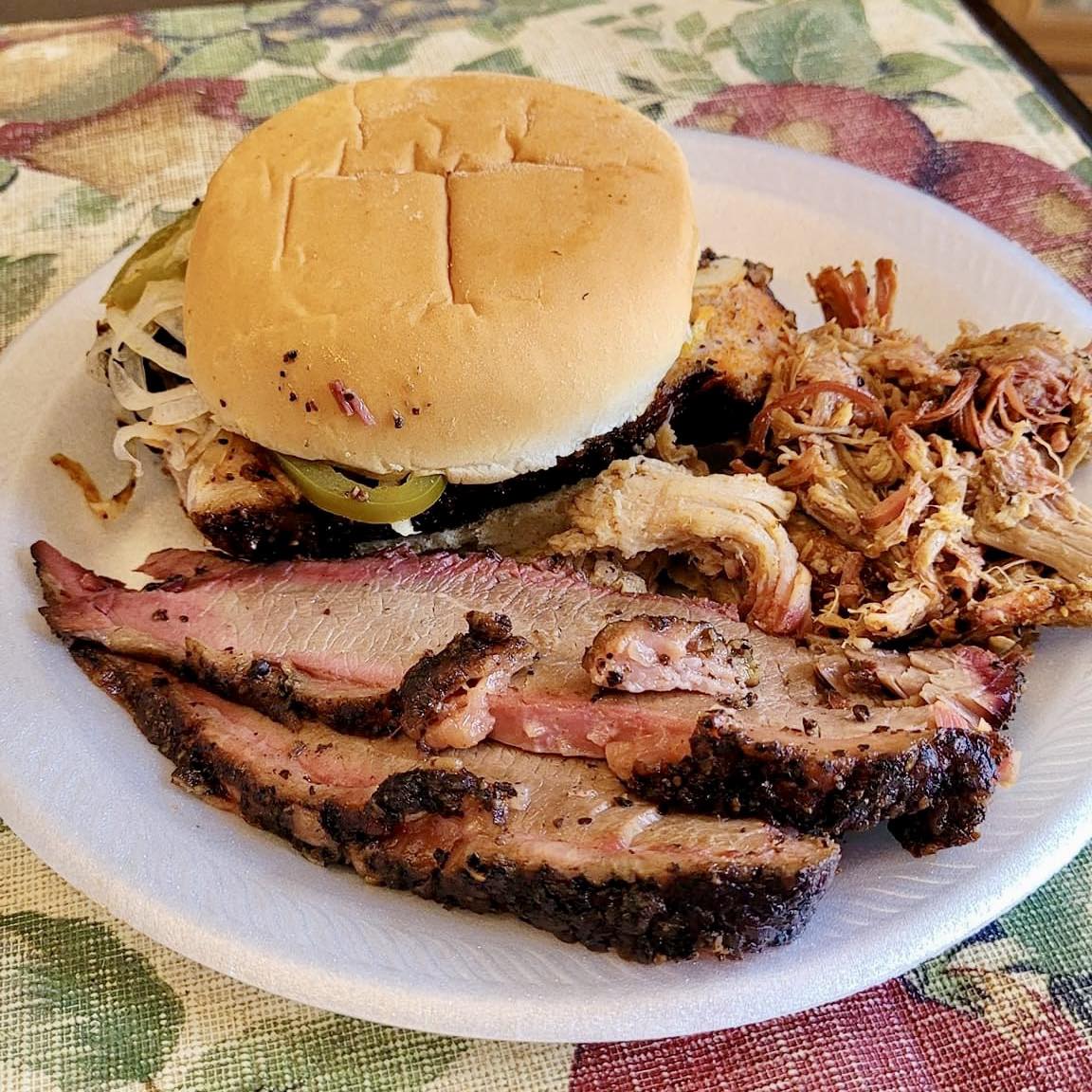 A plate of food with a burger, meat, and a pickle on a table.
