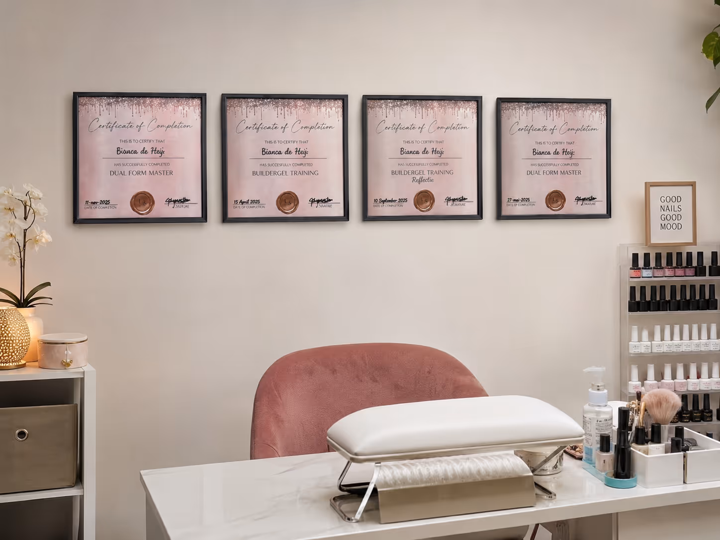 Nail salon workspace with pink chair, nail polish display, certificates, and manicure tools on white table.