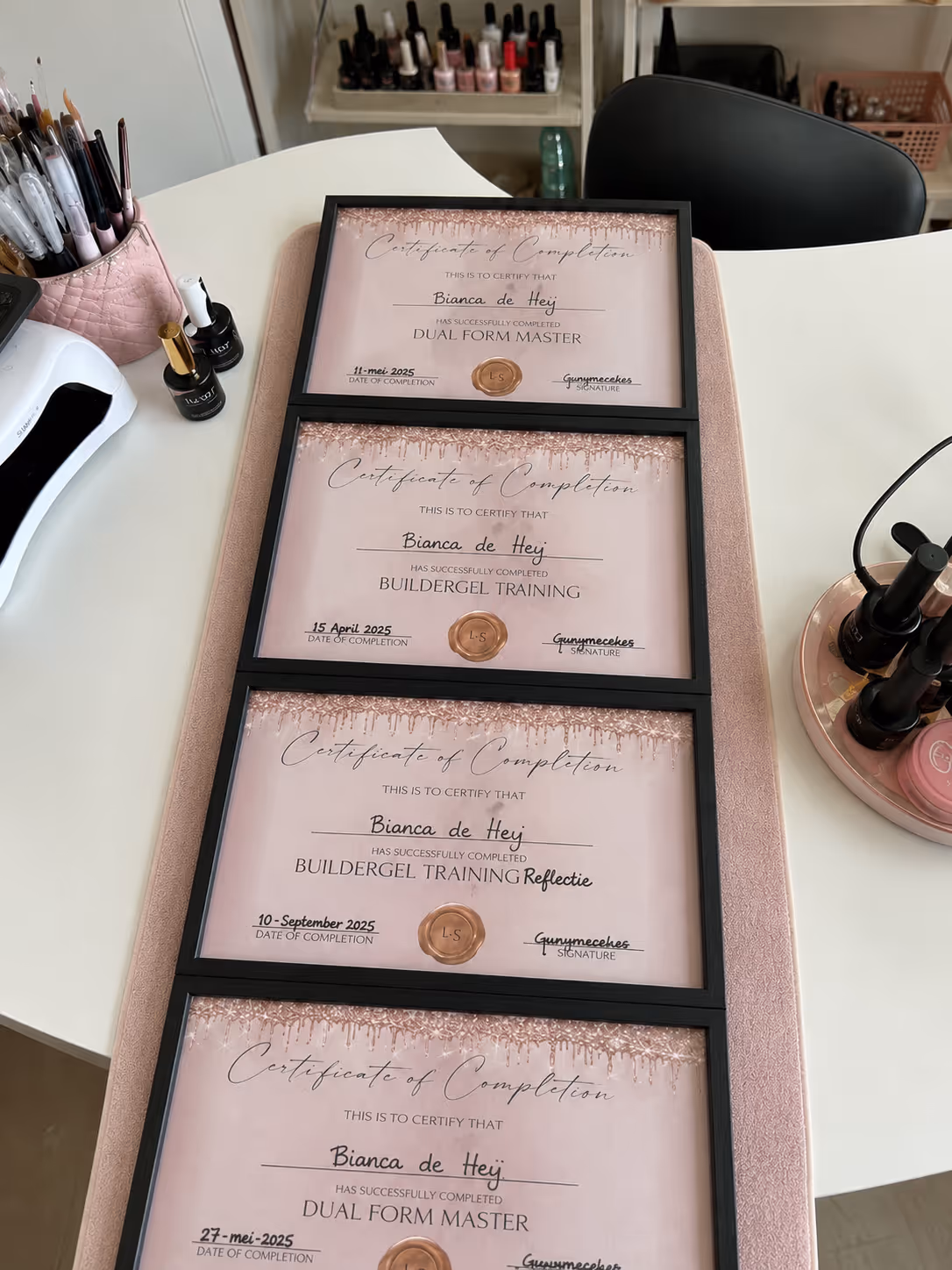Four framed certificates on a table, each certifying Bianca de Heij for nail training completions.