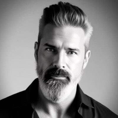 Black and white portrait of a bearded man with styled hair wearing a dark shirt.