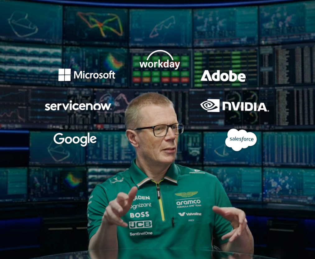 Man in green Aston Martin Aramco Formula One Team shirt speaking with hand gestures indoors.