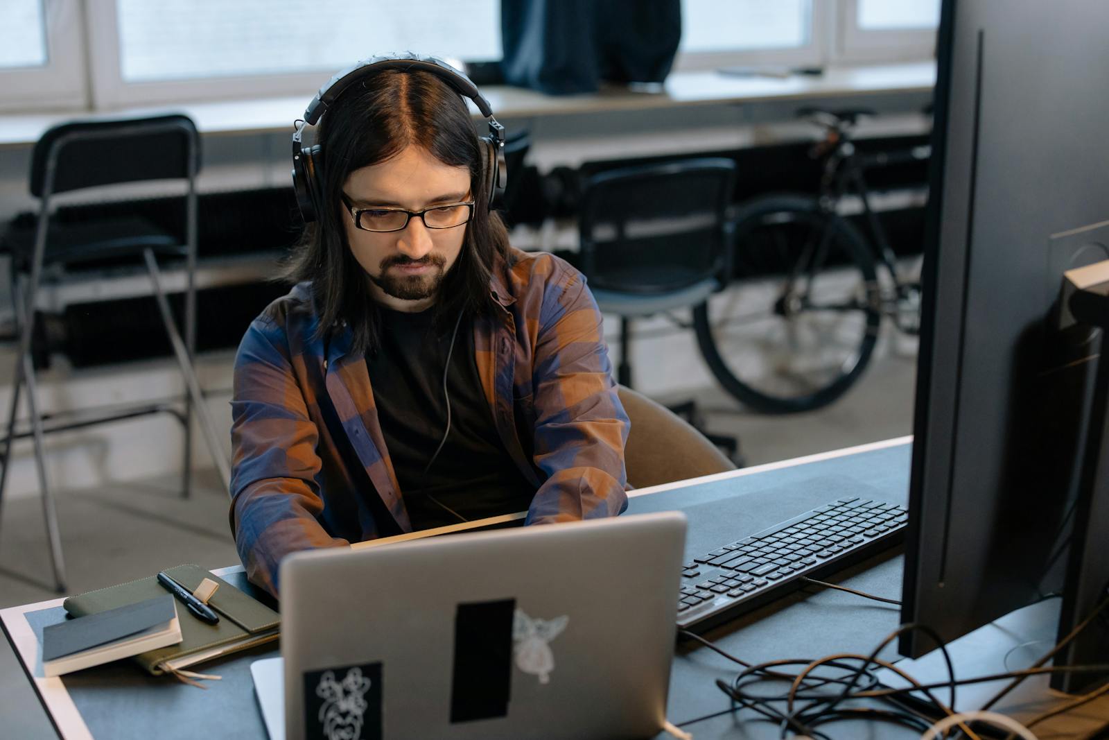 Bearded developer in headphones coding on a laptop in a modern office