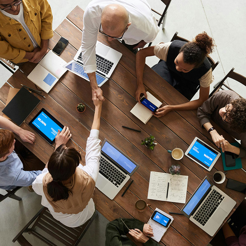 Professionals on a large desk in front of their laptops having a meeting and shaking hands