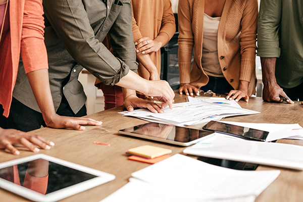 Professionals all pointing at documents and tablets on a table