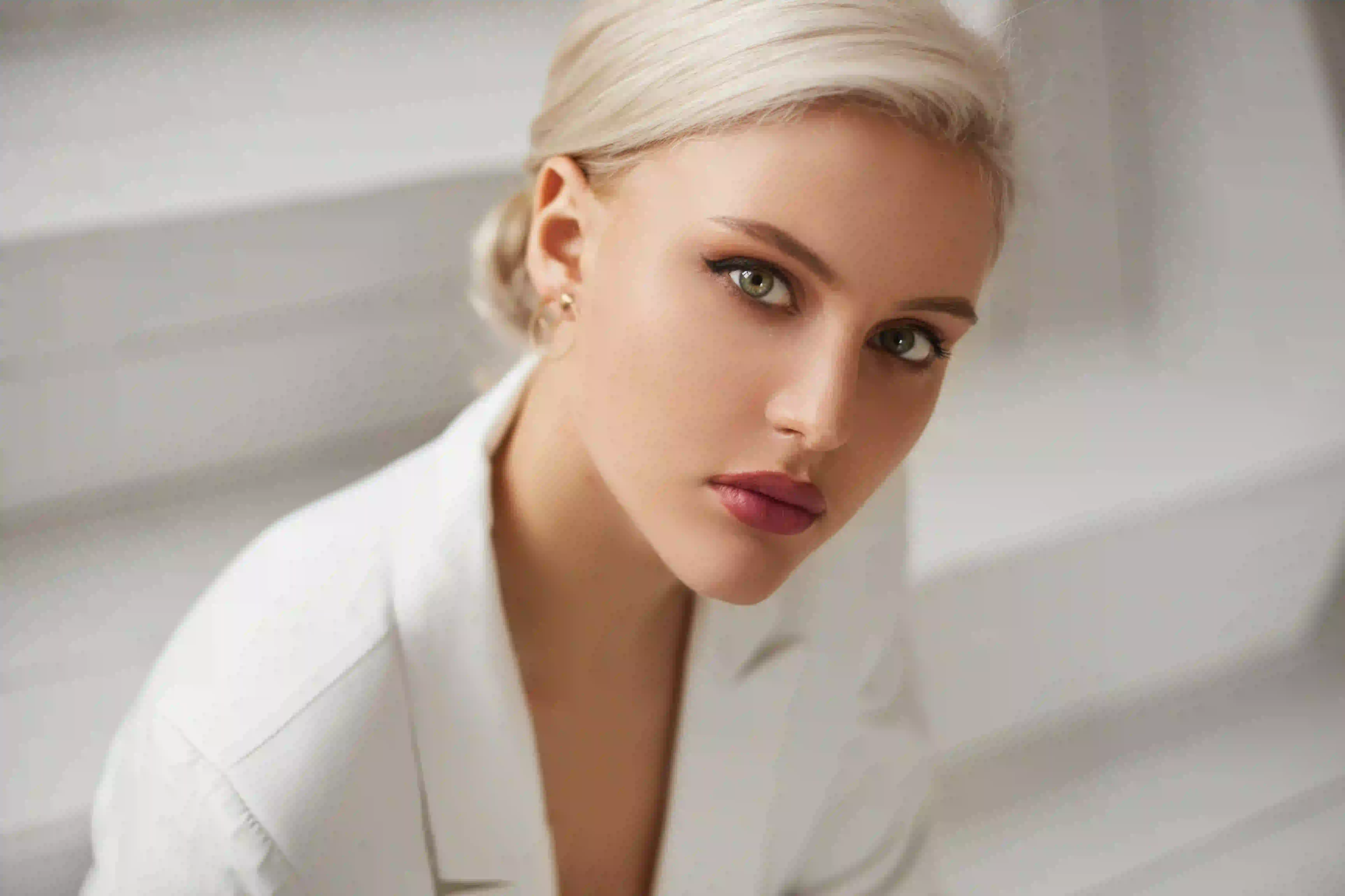 Close-up of a young woman with blonde hair and green eyes wearing a white shirt looking attentively at the camera.