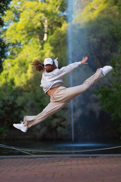 Dynamic female dancer executing a high split leap outdoors demonstrating flexibility and body movement mastery