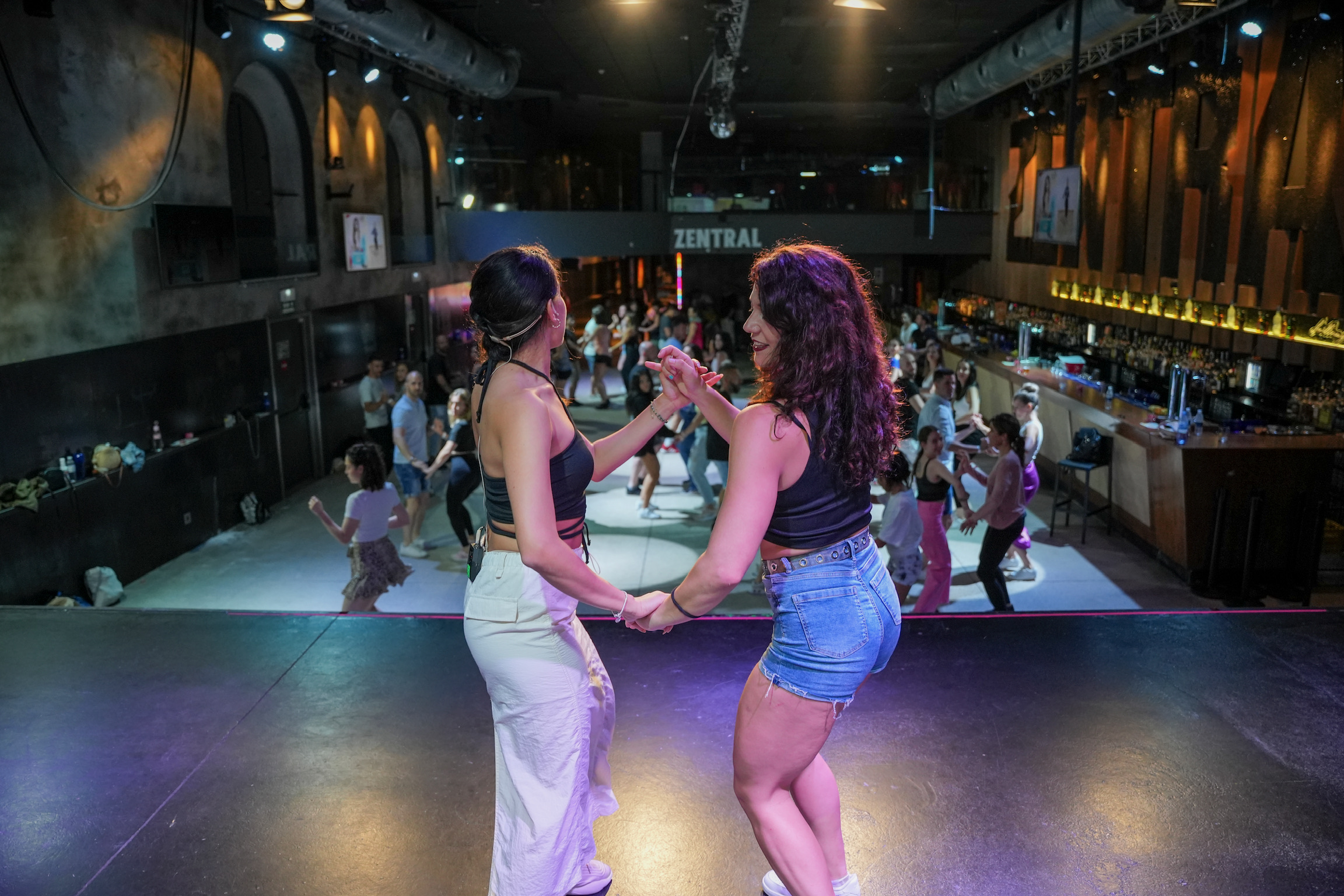 Two female dancers leading a bachata body movement workshop stage class in front of students