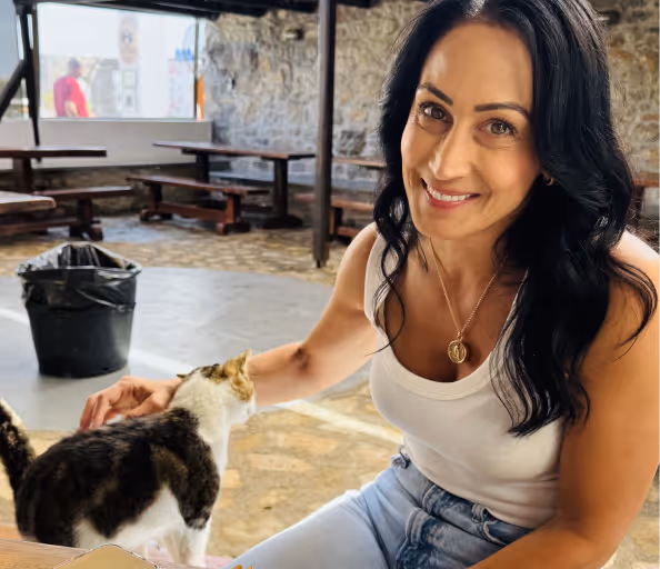 Woman with long black hair smiling and petting a black and white cat indoors near wooden benches.