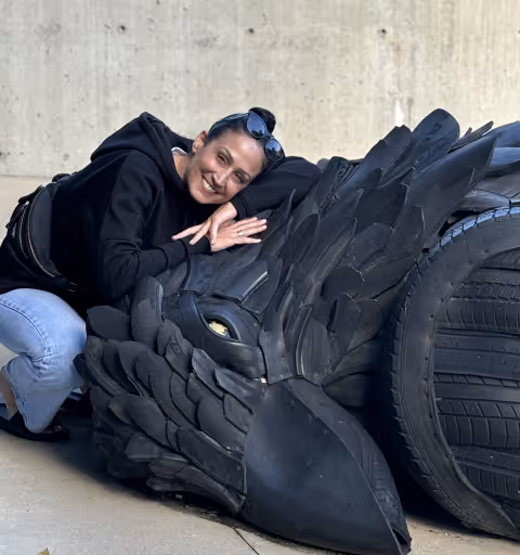 Woman leaning on a large black eagle sculpture made from recycled tires outdoors.