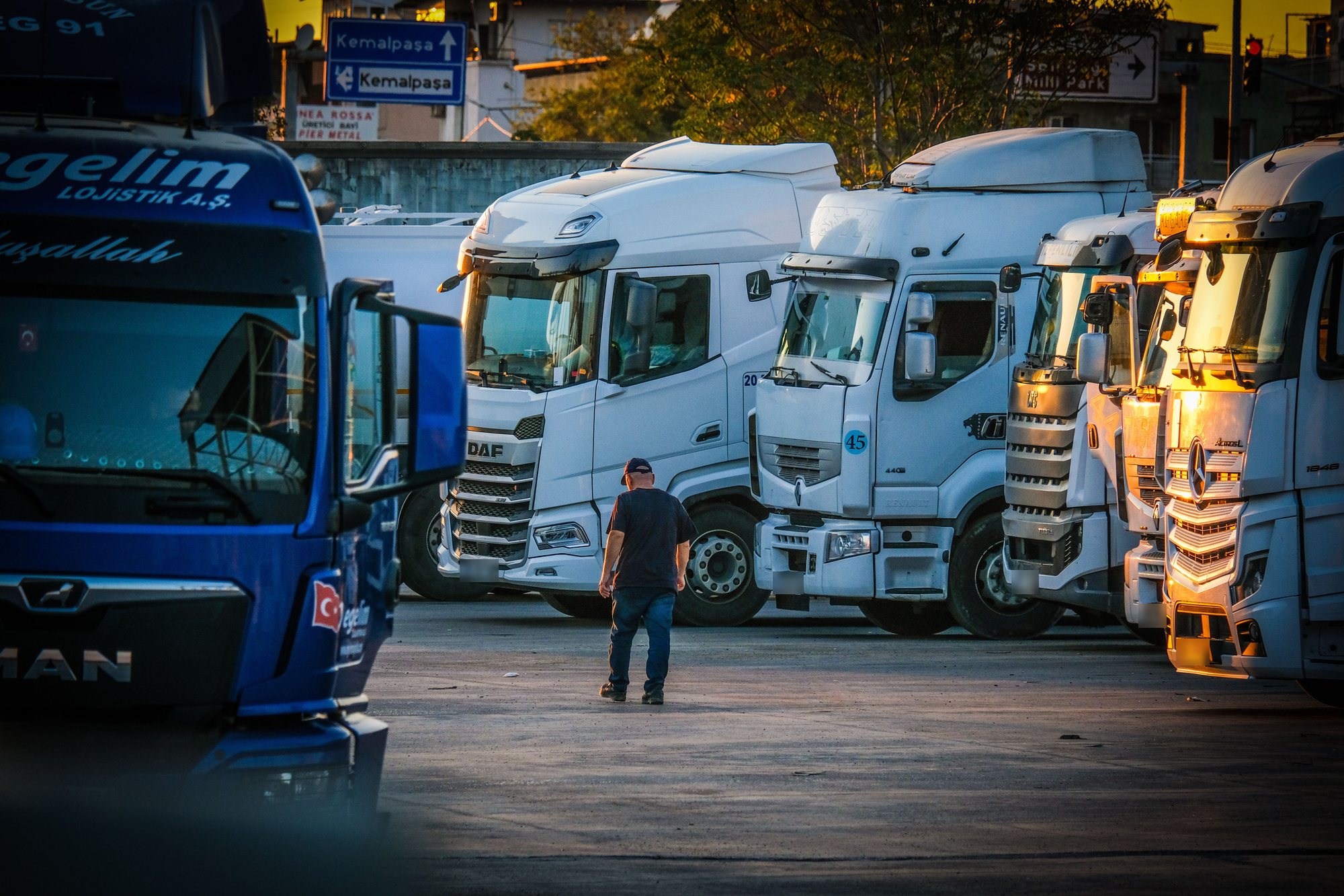 HGV drivers' yard at sunset with a row of parked trucks and a driver walking between them