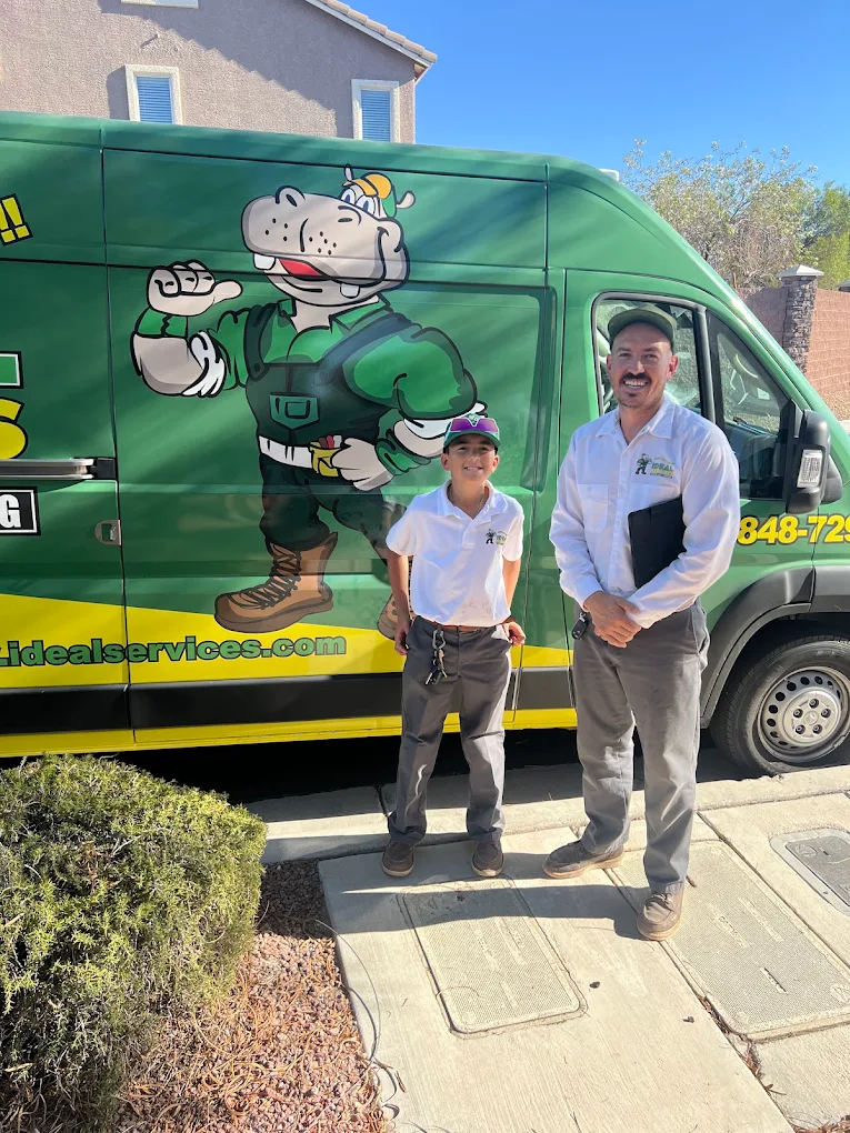 Two men in uniform standing in front of a green service van with a hippo mascot graphic.