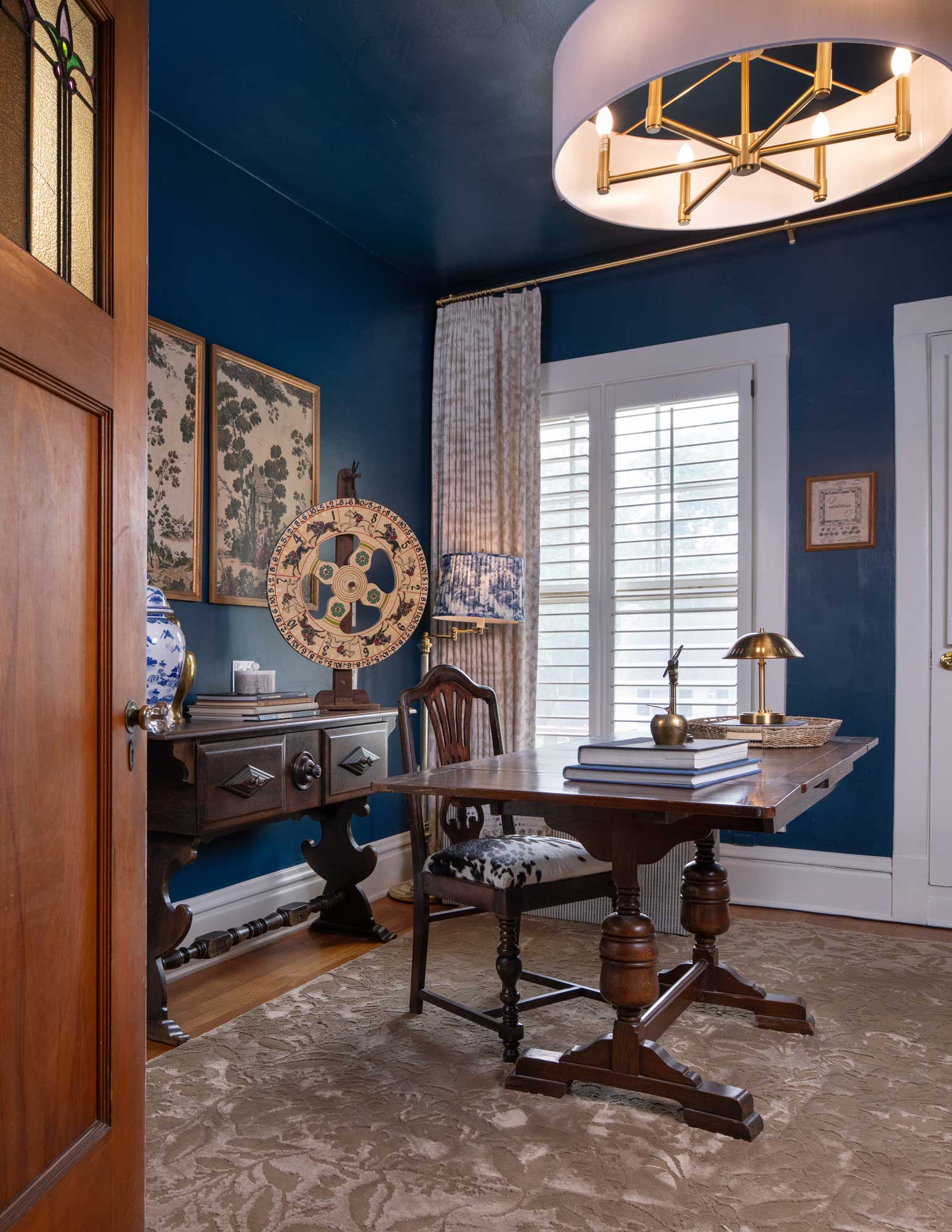 Traditional wood office with dark blue walls, wooden desk, chair, ornate rug, and decorative items.