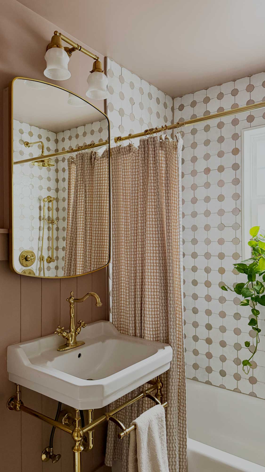 Bathroom with brass faucet, mirror, towel rack, beige shower curtain, and patterned tile walls.