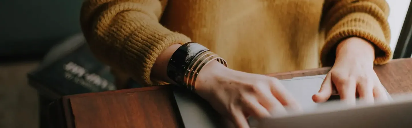 Hands typing on a laptop keyboard with a person wearing a brown sweater and bracelets.