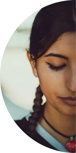 Close-up of a woman with braided hair, wearing makeup and a red pendant necklace.