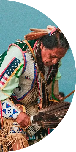 Native American man in traditional attire holding a feather fan, bowed head in ritual.