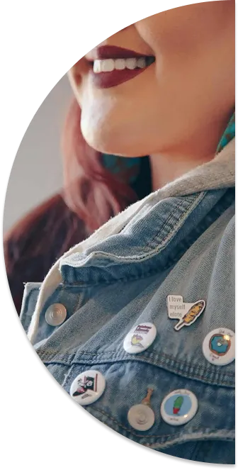 Close-up of a smiling person wearing a denim jacket adorned with multiple colorful pins.