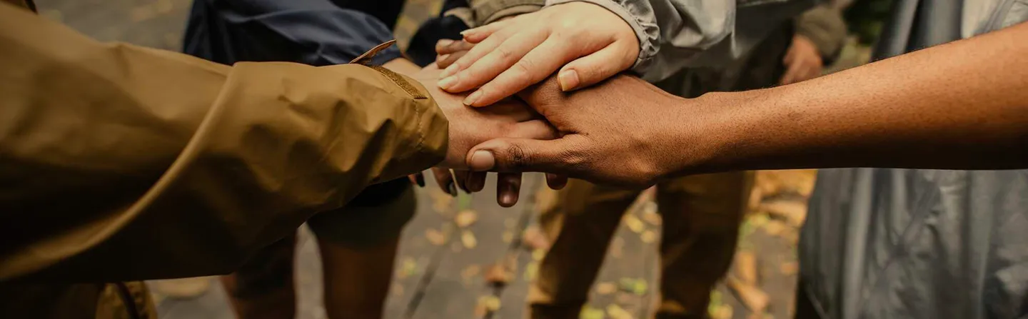 Diverse group of people stacking hands together in a gesture of unity outdoors.