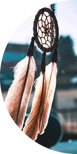 Close-up of a dreamcatcher with three large feathers hanging against a blurred background.