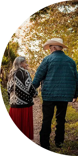 Elderly couple holding hands walking on a forest path with autumn leaves.