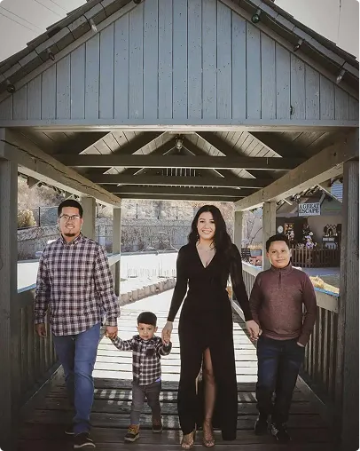 Family of four walking on a wooden covered bridge holding hands, with two children and parents.