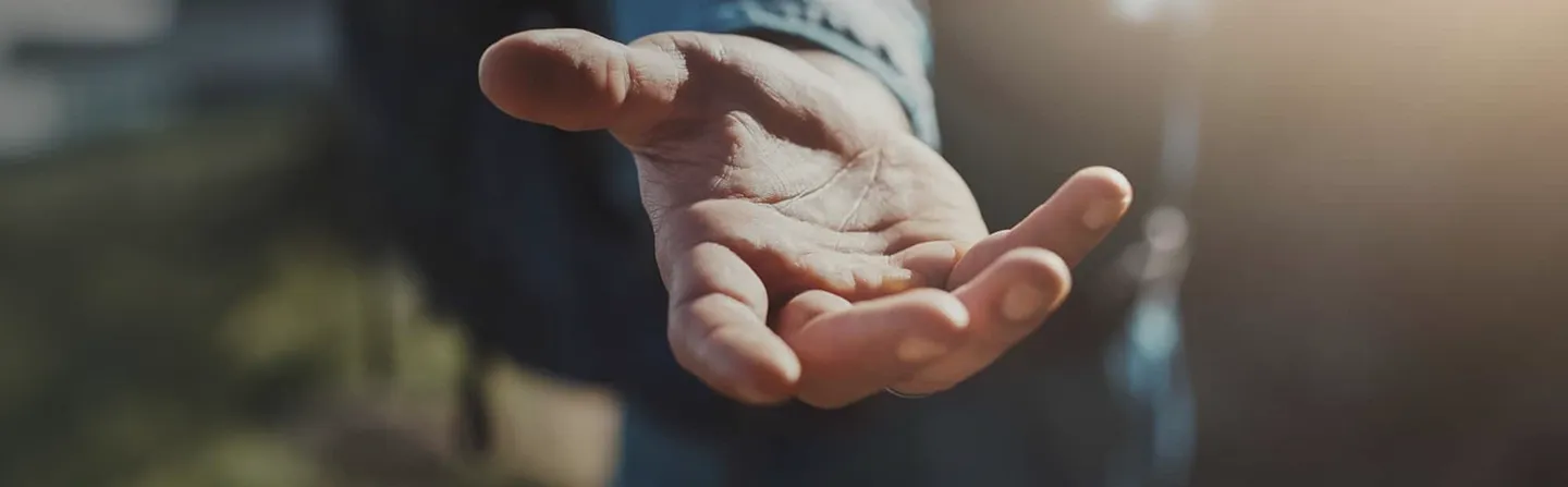 Outstretched hand reaching forward in soft natural light with blurred background.