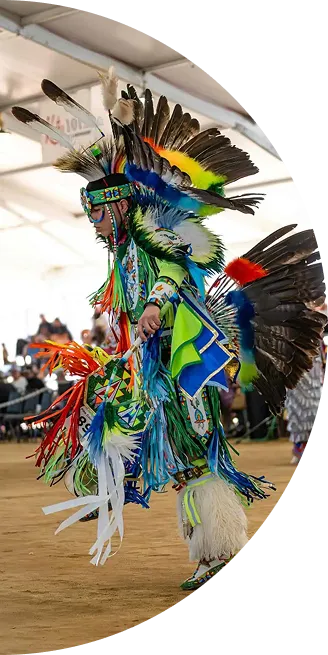 Native American dancer in colorful traditional regalia performing at a cultural event indoors.