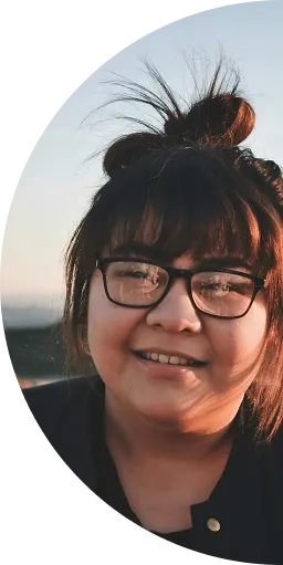 Smiling young woman with glasses and a messy bun hairstyle outdoors at sunset.