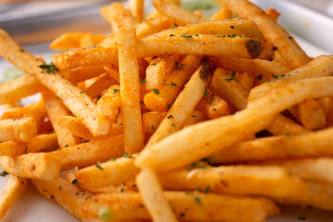 Close-up of seasoned French fries garnished with herbs on a white plate.