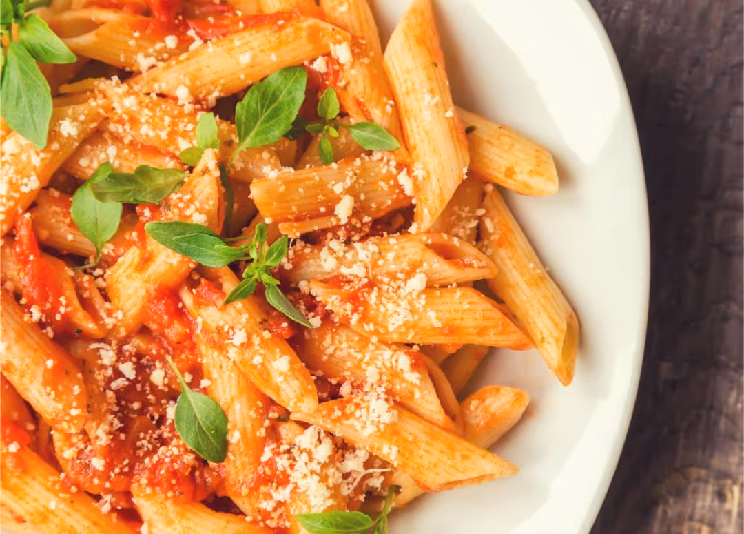 Penne pasta with tomato sauce, grated cheese, and fresh basil leaves on a white plate.