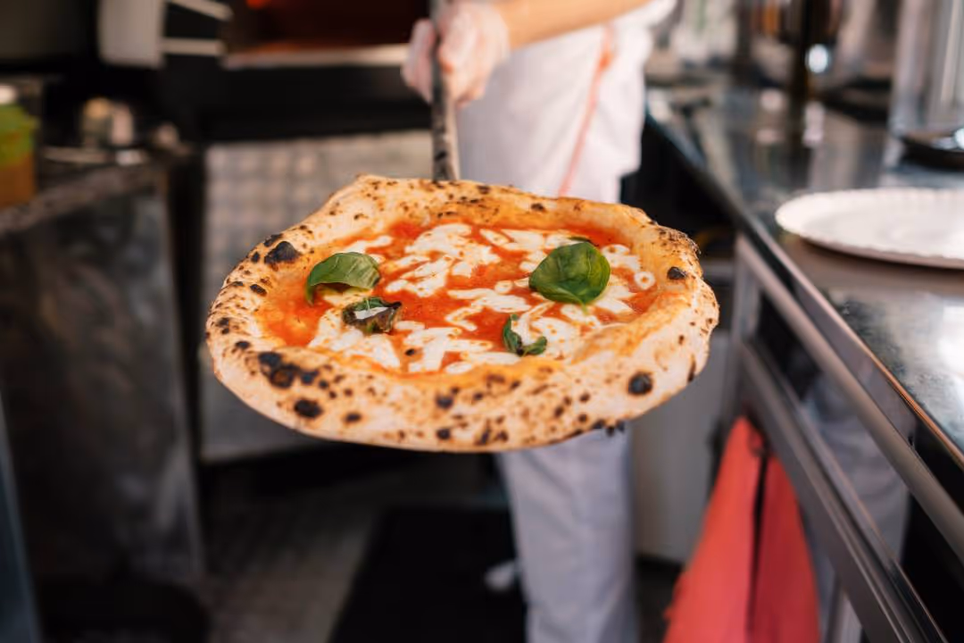 Freshly baked margherita pizza with tomato sauce, mozzarella, and basil leaves on a peel.