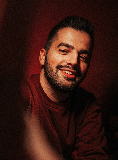 Smiling bearded man wearing a dark red sweater posing against a red background.