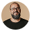 Headshot of a man with glasses and a beard wearing a black shirt, smiling on a white background.