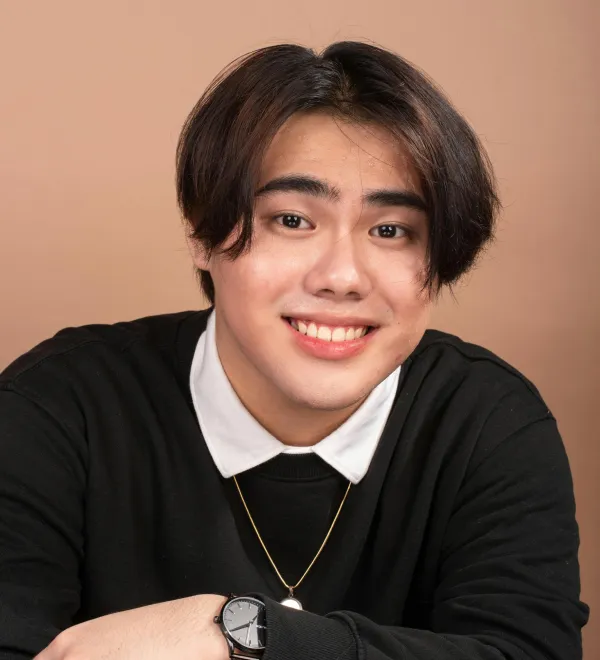 Smiling young person with medium-length dark hair wearing a black sweater and white collared shirt.