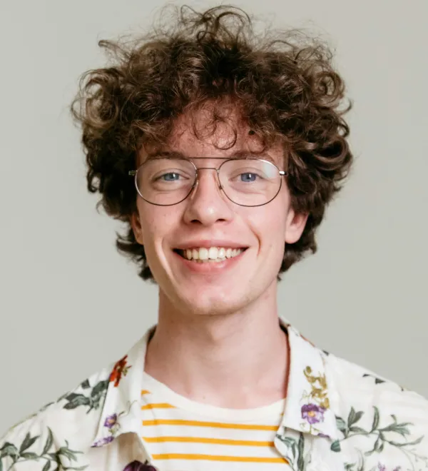Smiling young man with curly hair and glasses wearing floral shirt and striped T-shirt.