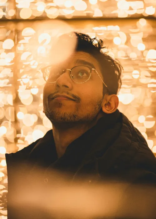 Man with glasses looking up with warm golden bokeh lights in the background.