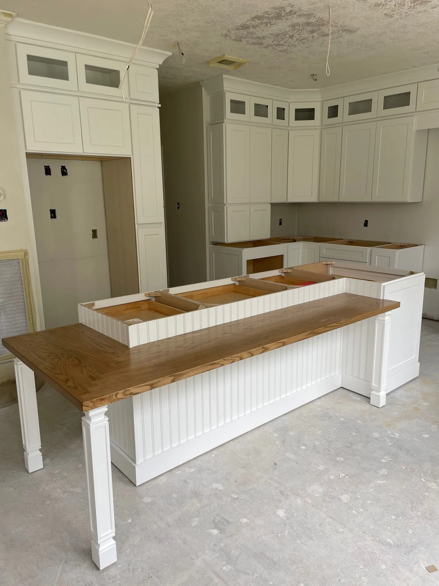 Unfinished kitchen with white cabinets and a wooden-top island under construction on a bare floor.
