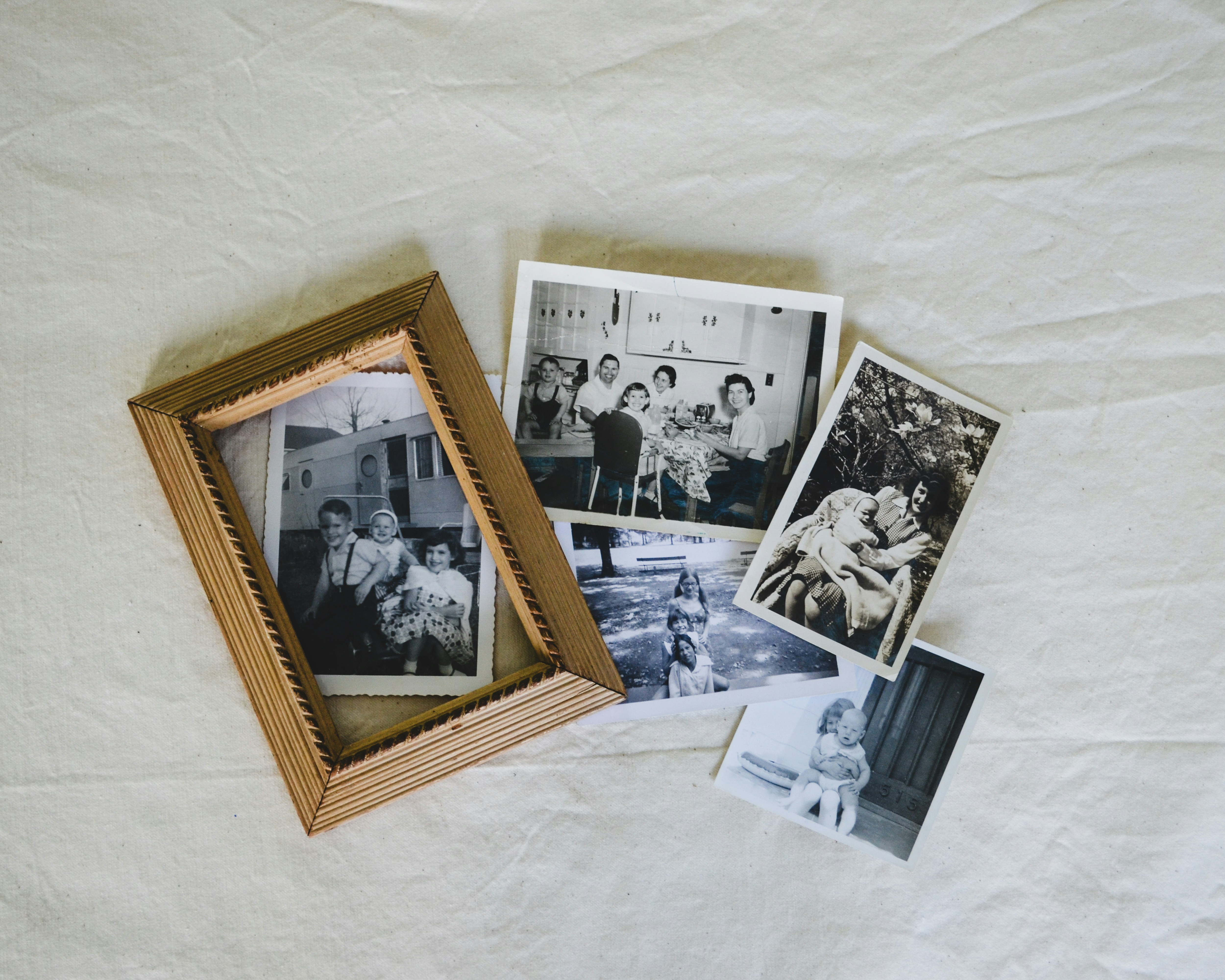 Vintage family photographs and a wooden picture frame arranged on cream fabric.
