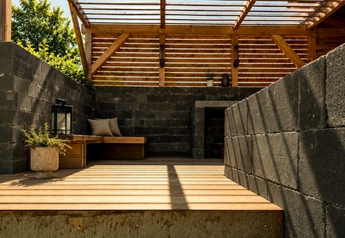 Überdachte Terrasse mit Holzdielen, Sitzbank mit Kissen und schwarzer Mauer aus Betonsteinen