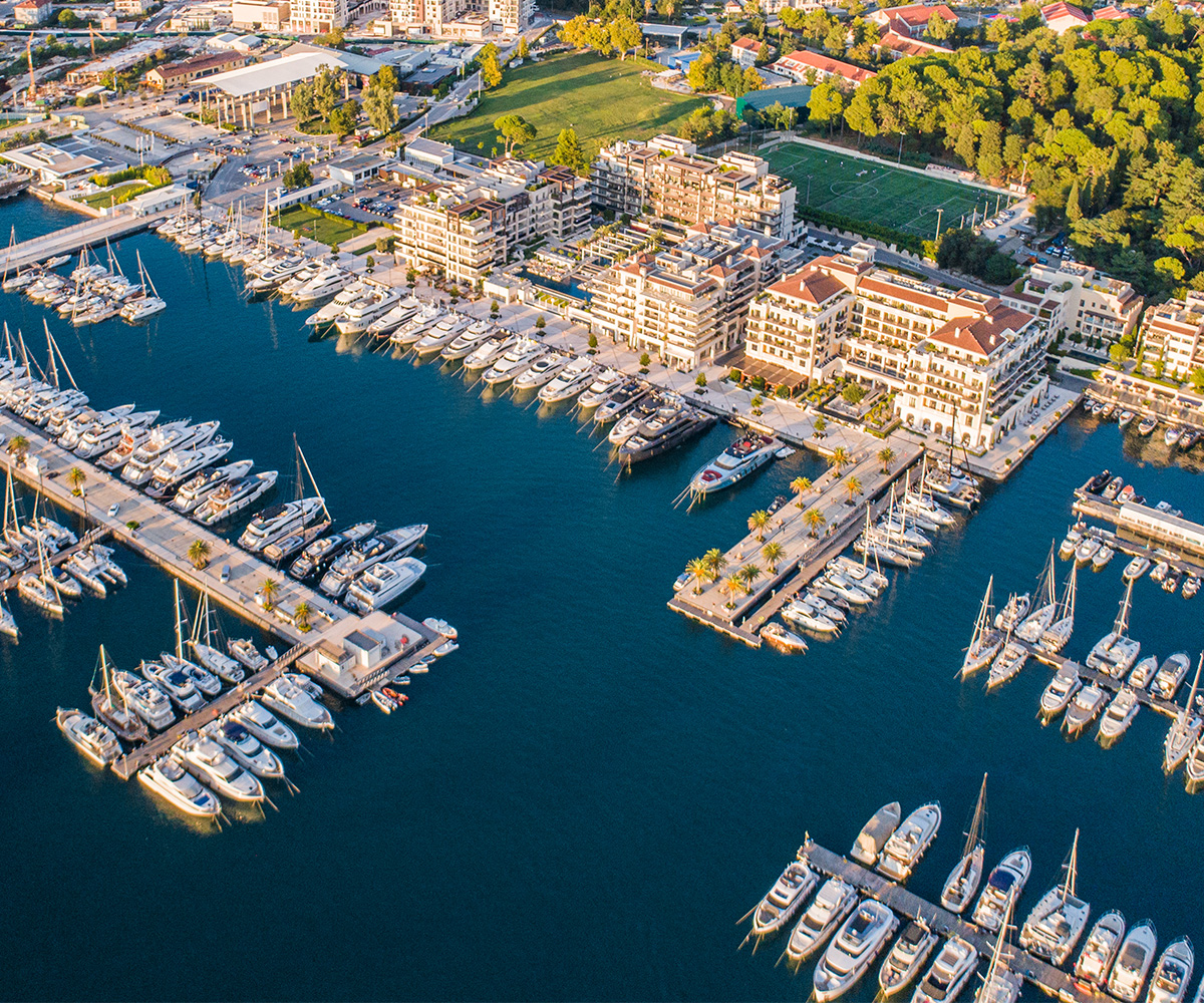 Aerial view of Platinum rated marina Porto Montenegro with superyachts docked next to waterfront buildings and green park area.