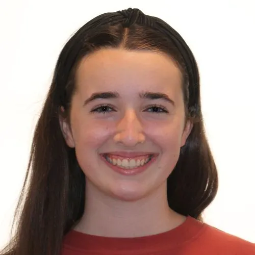 Smiling young woman with long dark hair wearing a red top and black headband against white background.