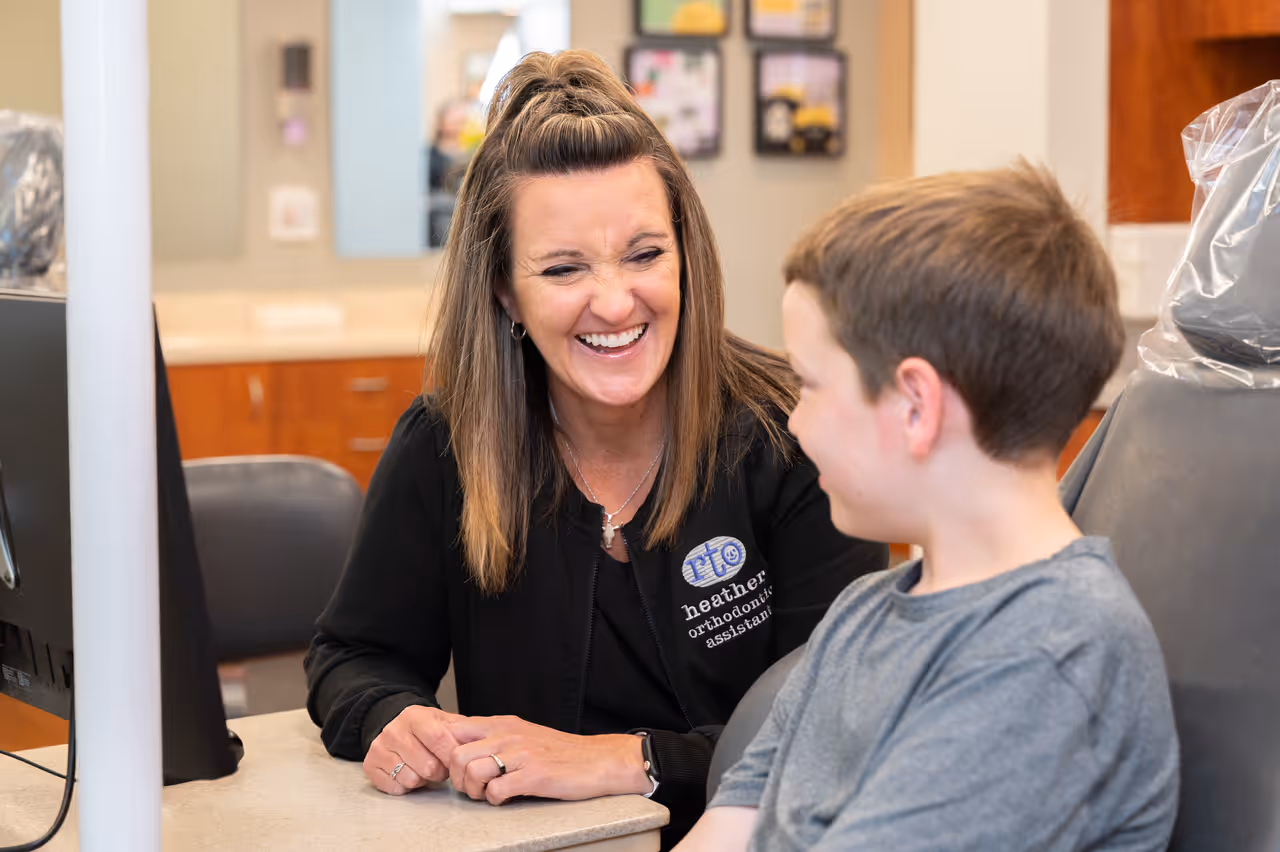 Smiling orthodontic assistant talking to a boy sitting in a dental chair.