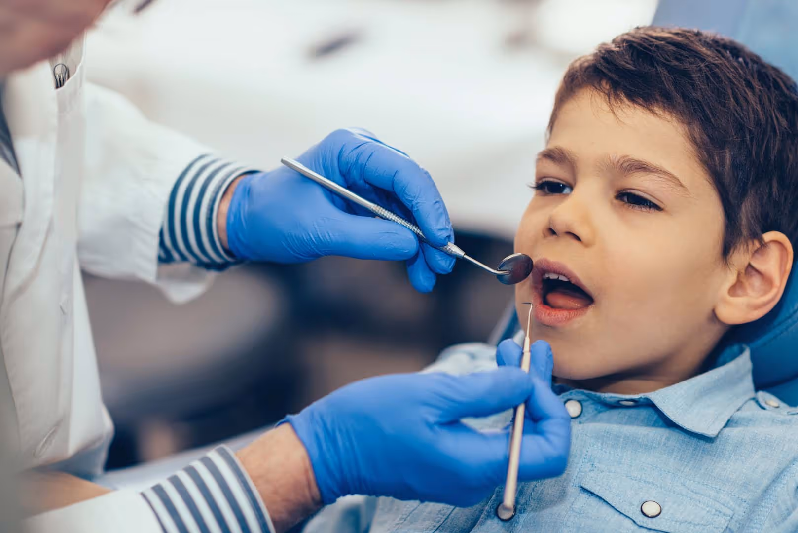 Young boy receiving dental checkup from dentist wearing blue gloves using dental tools.