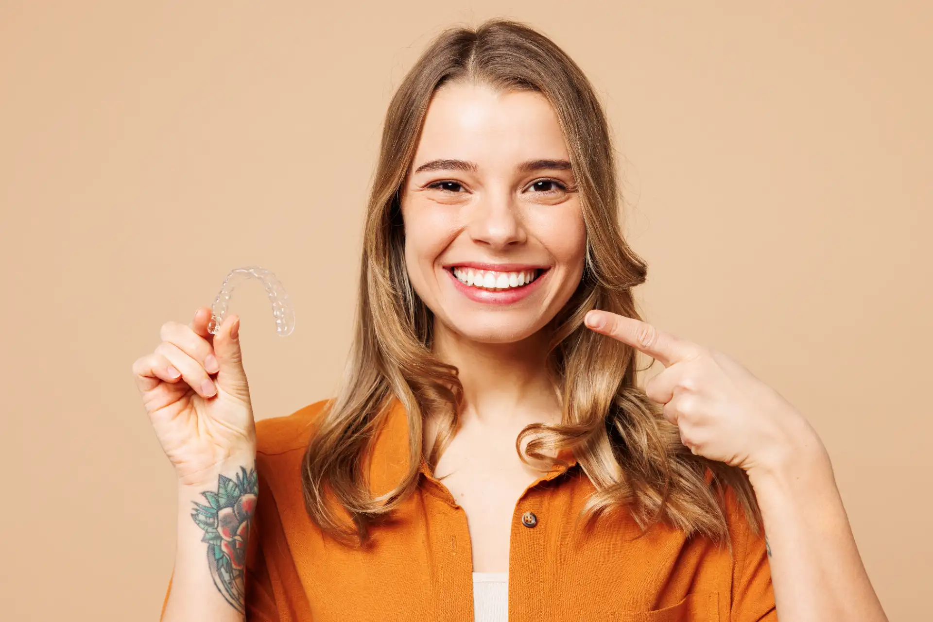 Smiling woman holding a clear dental aligner and pointing to her teeth.
