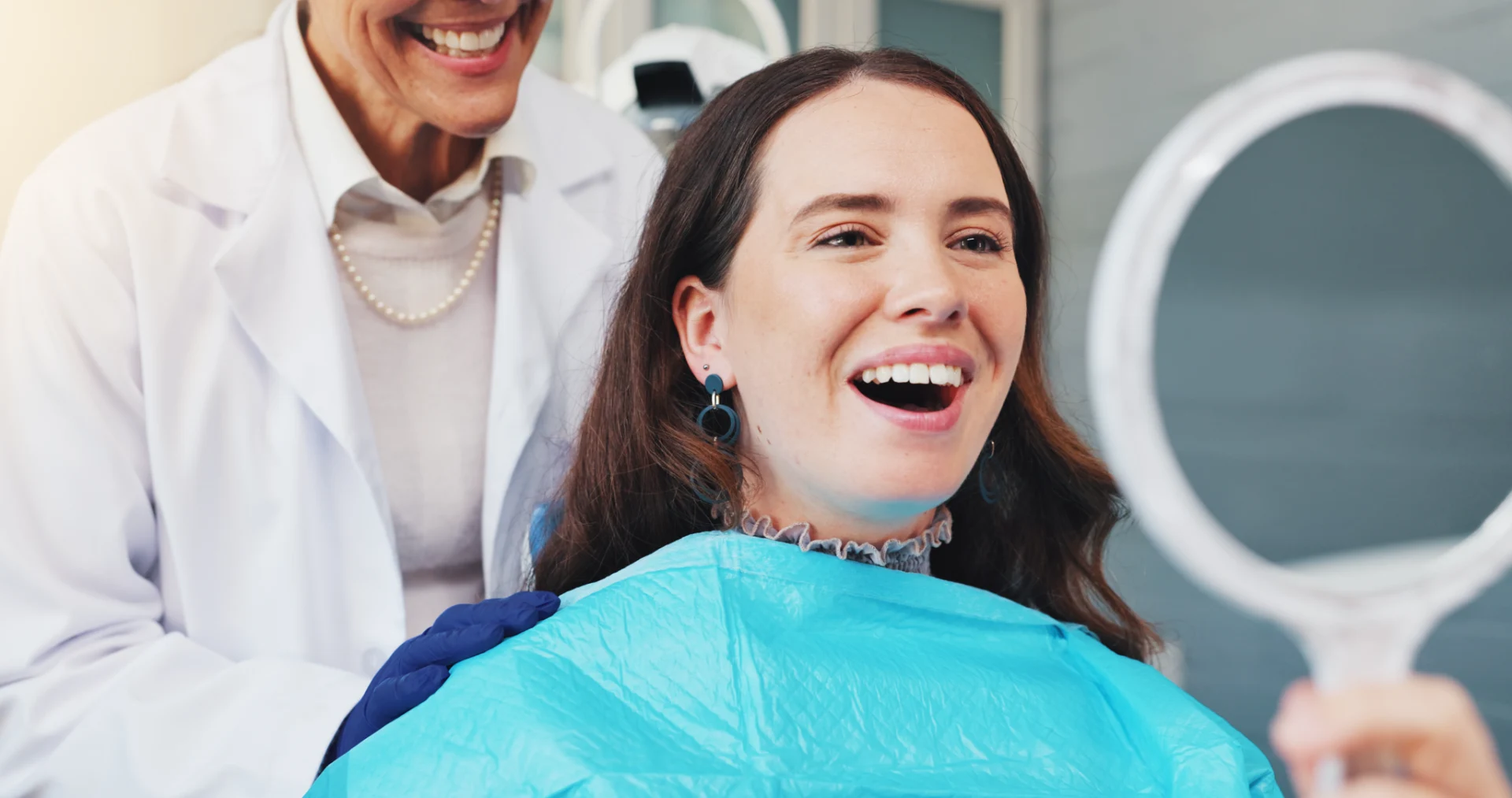 Woman in dental bib smiling with dentist wearing gloves and white coat behind her.