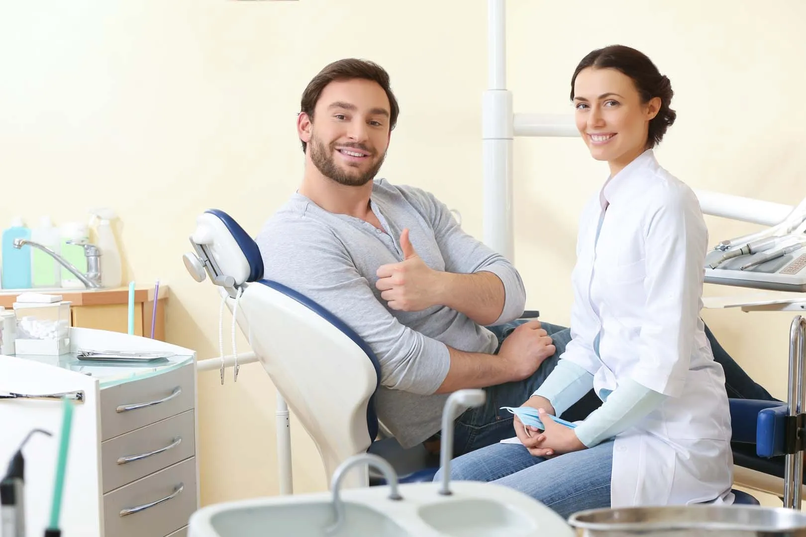Smiling man giving thumbs up in dental chair with a female dentist beside him in a clinic.